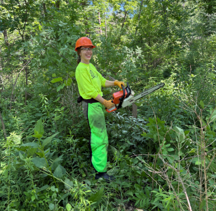 A woman in full chainsaw gear in the woods